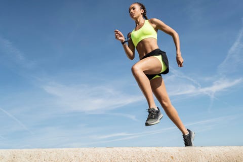 Low angle view of young female runner running along sea wall against blue sky