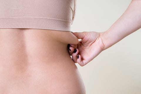 Woman holding fold of skin, cellulite on female body, beige background