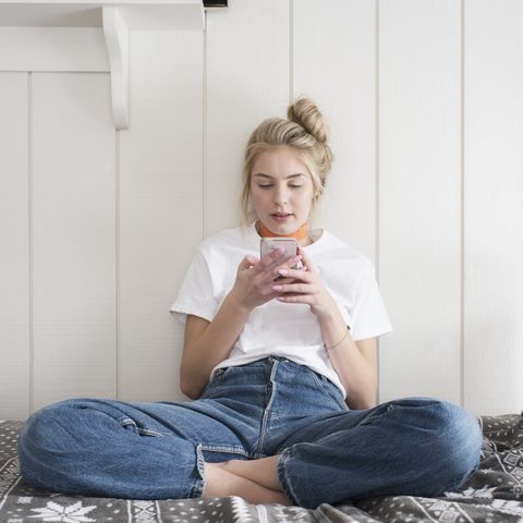 Teen girl with phone sitting on bed