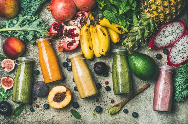 flat lay of colorful smoothies in bottles with fresh tropical fruit and superfoods on concrete background, top view healthy, clean eating, vegan, vegetarian, detox, dieting breakfast food concept