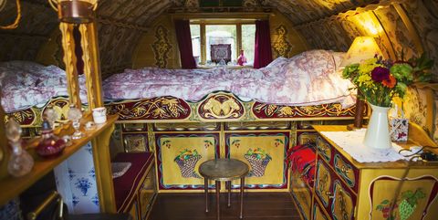 the interior of a traditional gypsy caravan with raised bed and cupboards, bow top roof and stove