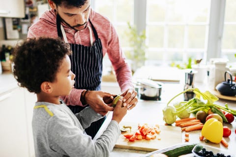 Ein Vater zeigt seinem Sohn zu Hause in der Küche sorgfältig, wie man Obst schält und Gemüse schneidet