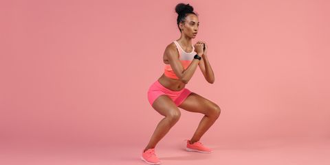 sporty woman practicing squat exercises in studio african woman in sportswear working out on pink background