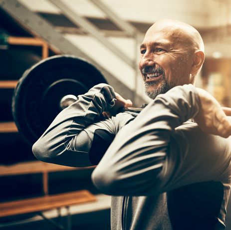 Fit mature man lifting weights and smiling in a gym