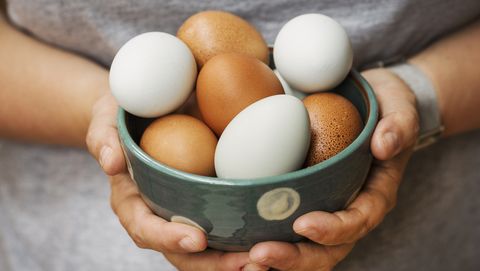 A woman holding bowl with fresh brown and white eggs.