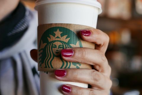 Hand holding a coffee cup in a Starbucks coffee shop. In...