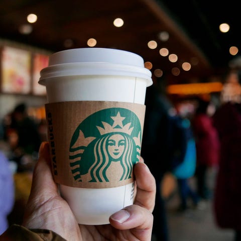 Hand holding a coffee cup in a Starbucks coffee shop. In Hand holding a coffee cup in a Starbucks coffee shop. In