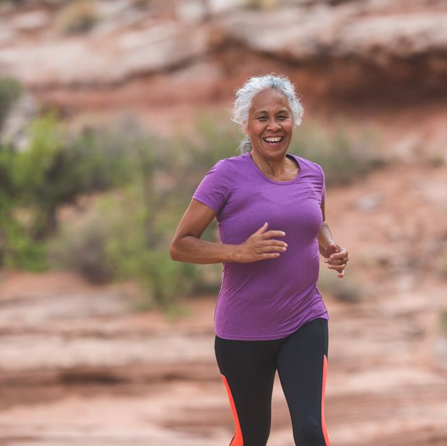 a senior ethnic woman goes for a solo run in the utah desert on a sunny afternoon she has a big smile and looks happy as she runs along a trail surrounded by boulders, rocks, sandstone, and sagebrush