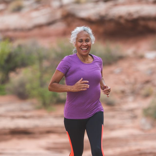 a senior ethnic woman goes for a solo run in the utah desert on a sunny afternoon she has a big smile and looks happy as she runs along a trail surrounded by boulders, rocks, sandstone, and sagebrush