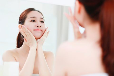 Young woman looking in mirror, touching face