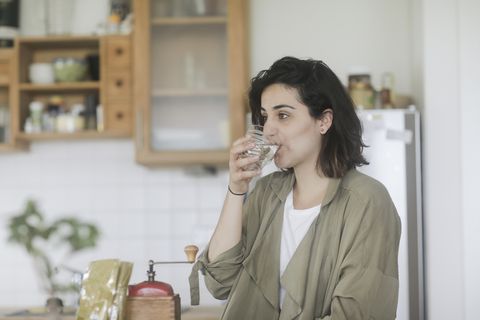 Woman standing in the kitchen drinking a glass of water