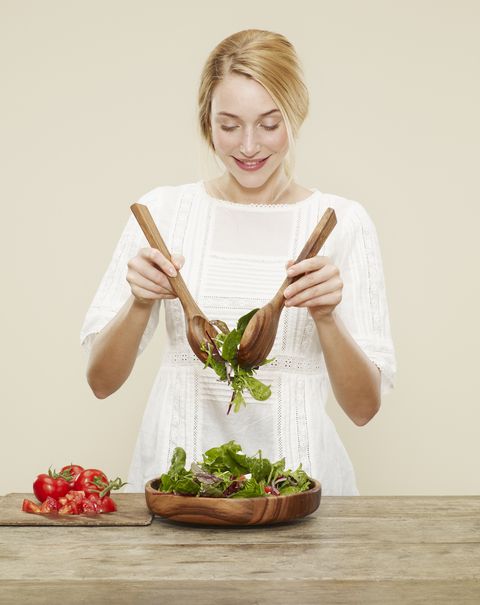 female, blonde hair, blue eyes, smile, white dress,fresh salad, salad bowl, mixing tongs mixed leaf, sliced tomoatoe, cutting board, biscuit background, yellow background