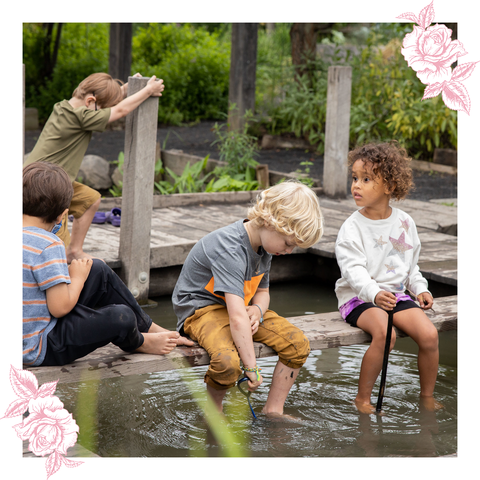 children sit on a dock with their feet in the water at the ithaca children's garden