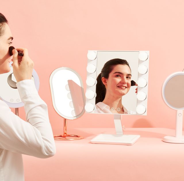 a woman applying blush in a vanity mirror, good housekeeping's picks for the best vanity mirrors with lights