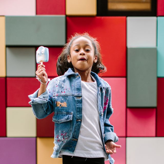 girl with popsicle jumping up against colorful tile background