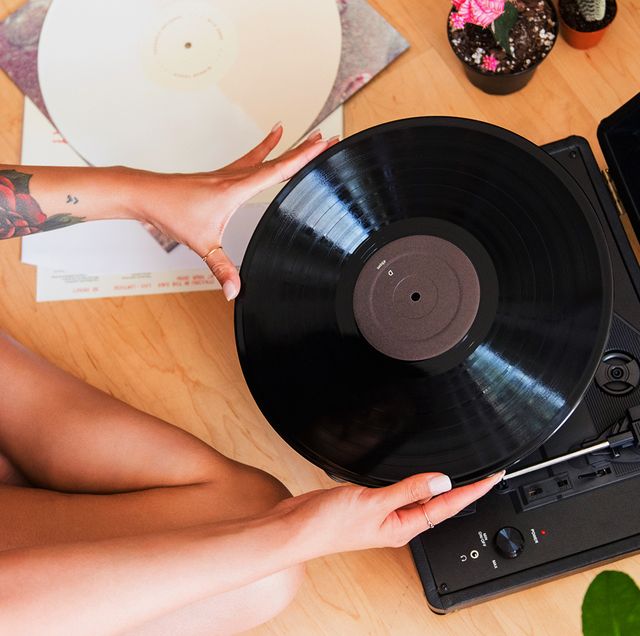 woman with tattoos sitting on bedroom floor putting record on turntable