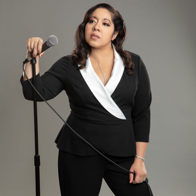 gina brillon wearing a black and white suit holding a microphone