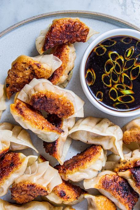 ginger pork potstickers next to a small bowl of soy sauce garnished with green onions