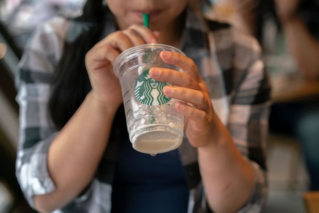 a girl drinks a starbucks coffee with a plastic straw