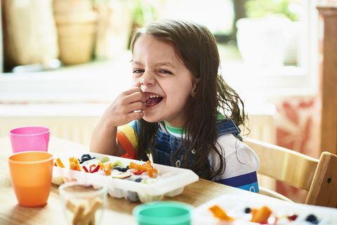 una niña sonríe mientras toma un snack saludable compuesto por crudités de verduras