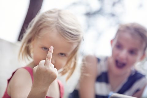 Girl holding up a middle finger, with shocked sibling in the background