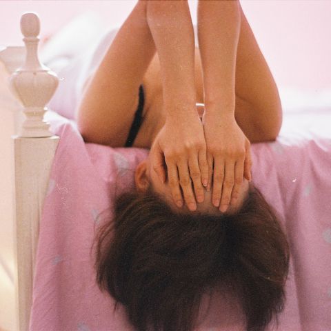 girl lying on the bed covering face by hand