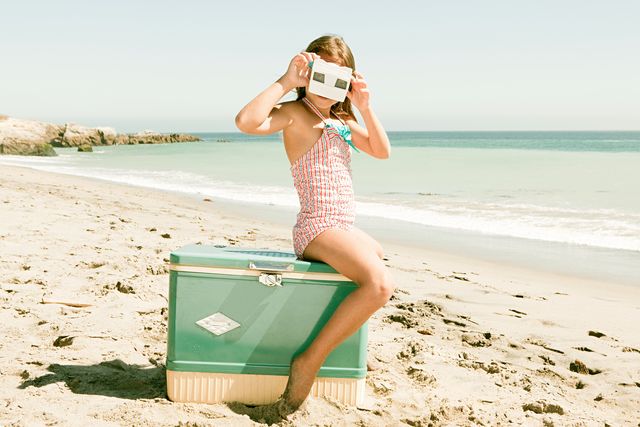 girl sitting on coolbox on beach looking through slide viewer