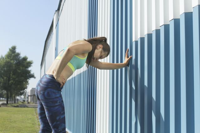 girl training, resting against blue wall, city