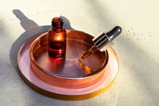 glass bottle of oil with a pipette or face serum on a concrete background with sunlight