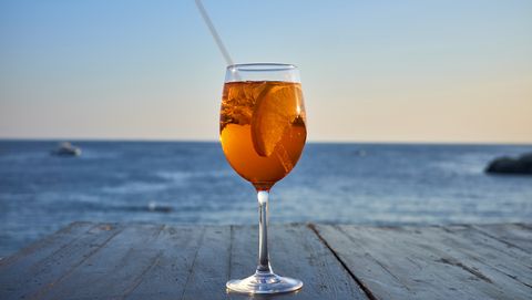Glass of ice-cooled Spritz with orange slice in front of the sea