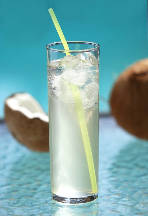 glass of iced coconut water with a cracked coconut shell behind it on a outside patio table by a swimming pool part of a series