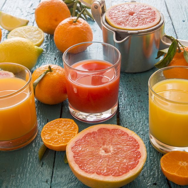 glasses of orange juice, grapefruit juice and multivitamine juice, juice squeezer and fruits on wood