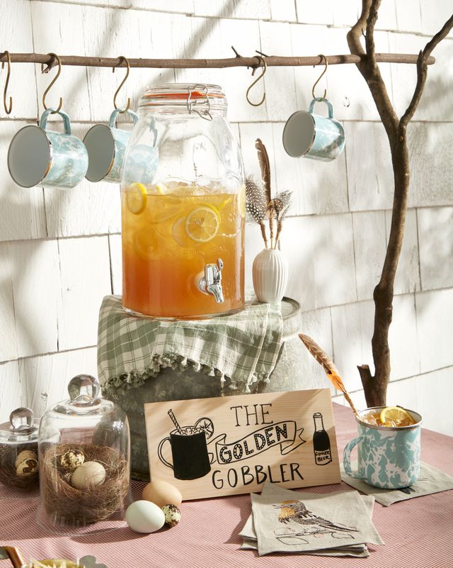 golden gobbler cocktail in a big pitcher jar on a table with a sign and cups hanging above from a wooden dowel