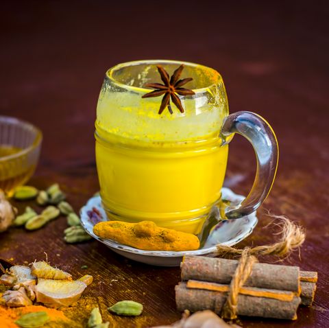 Golden milk with species like green cardamom,turmeric,cinnamon,honey and ginger on wooden surface.
