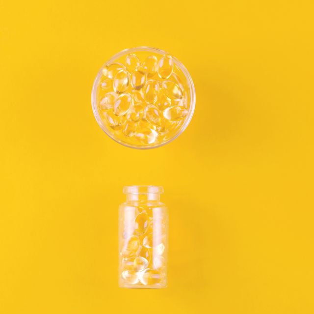 golden omega capsules in a bowl and bottle on yellow background, flat lay