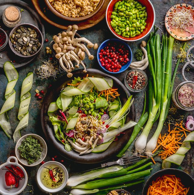 healthy vegan lunch bowl making detox beautiful buddha bowl with various fresh vegetables, edamame beans, mushrooms, seasoning and pumpkin seeds and nuts topping on rustic table with ingredients top view food flat lay