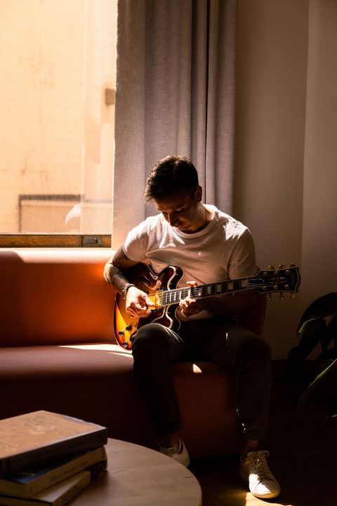 man sitting on couch while playing guitar wearing nomos watch on wrist
