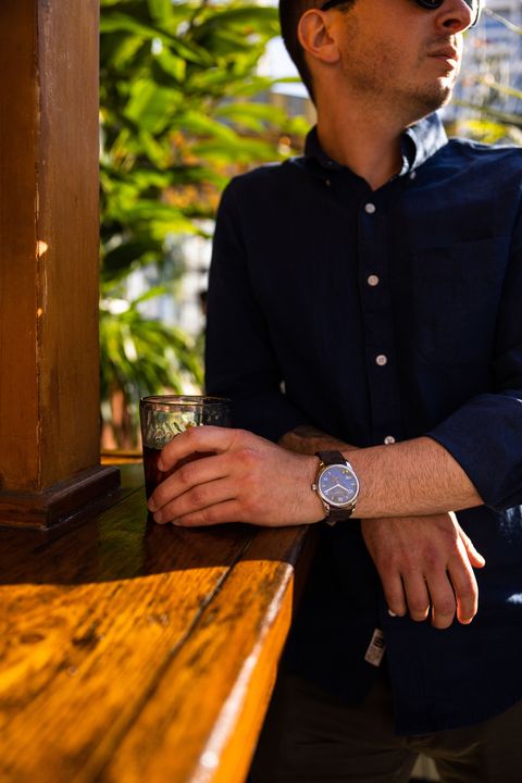 man leaning against bar while looking into the distance and holding a drink wearing nomos watch on wrist