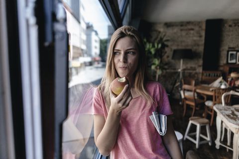 Young woman leaning on window, eating apple