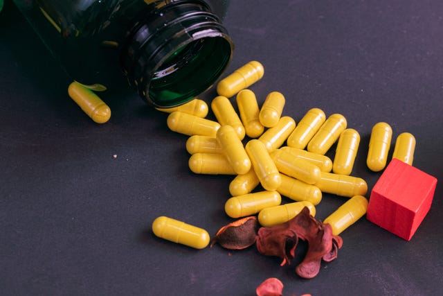 green bottle of supplements with yellow capsules on a black background