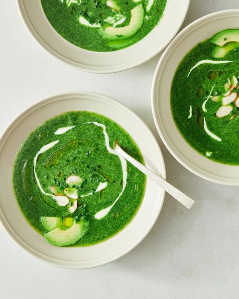 bowls of green goddess soup garnished with yogurt drizzle, avocado slices, and sliced almonds