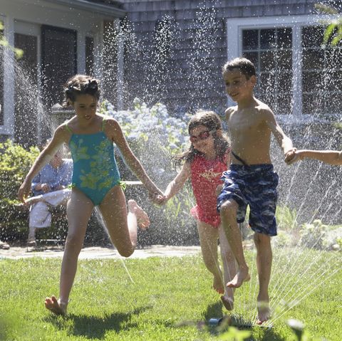 group of four children playing around a sprinkler in a garden