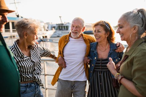group of happy senior friends tourists standing in city port, talking