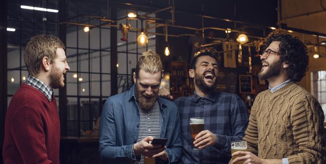 group of men having a laugh at the pub while drinking beer and watching a football game on the mobile phone