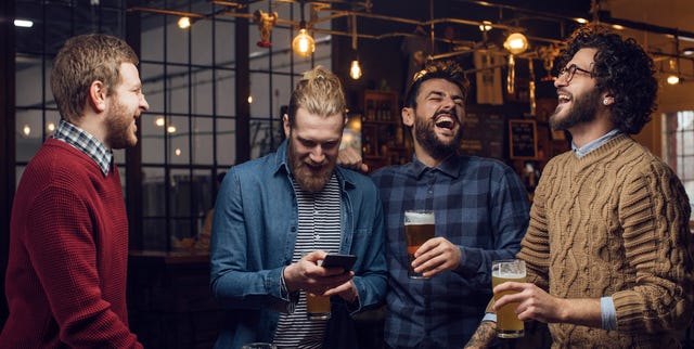 group of men having a laugh at the pub while drinking beer and watching a football game on the mobile phone