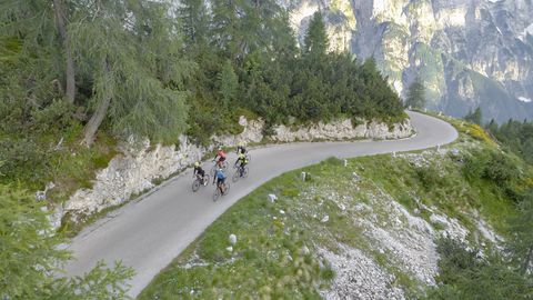 Group of road cyclists riding on beautiful mountain road surrounded by trees and mountains