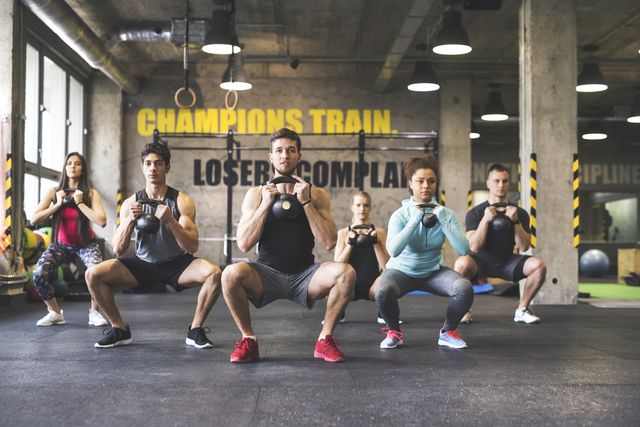 group of young fit people lifting kettlebells in gym