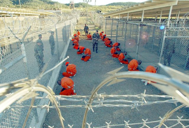 taliban prisoners in orange jumpsuits sitingt in holding area under the watchful eyes of military police at camp x ray at naval base guantanamo bay, cuba, during in processing to the temporary detention facility on jan 11, 2002 the detainees will be given a ba sic physical exam by a doctor, to include a chest x ray and blood samples drawn to assess their health    photo by shane mccoygreg mathiesonmaigetty images