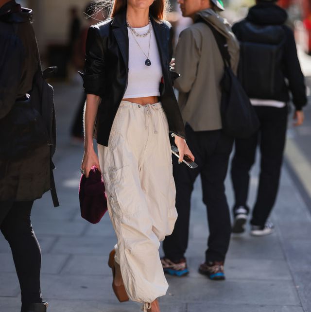 a fashion show attendee wearing ivory parachute pants with a cropped white tee and black blazer on the street during london fashion week september 2022