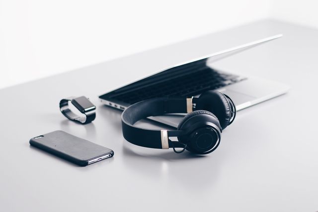 electronics on a white surface laptop, headphones, smart watch, and cell phone